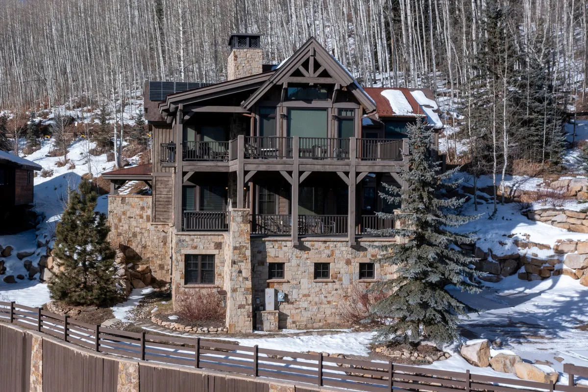The elegant stone facade of the home, accented by multiple balconies overlooking a snow-laden landscape and tall pine trees. The setting is peaceful, with hints of outdoor gathering spaces ideal for winter relaxation and nature appreciation.