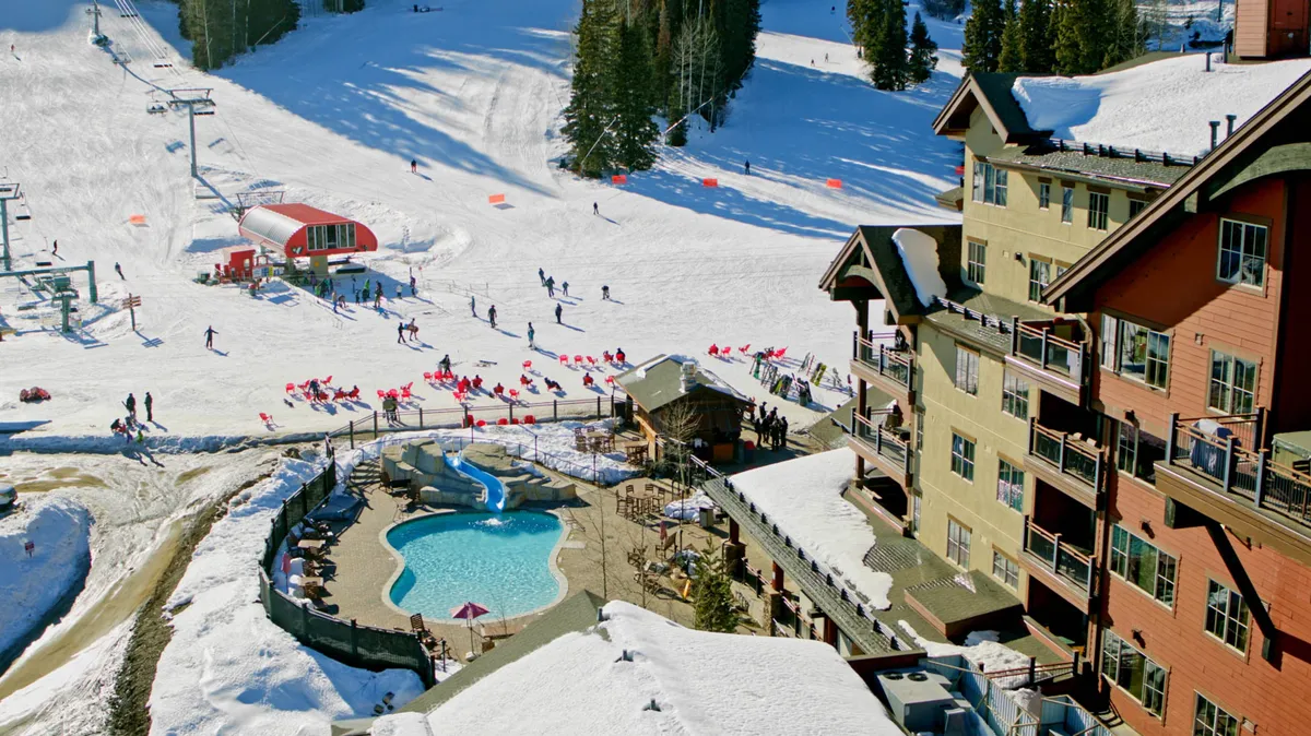 A vibrant winter scene featuring the ski slopes at Purgatory Resort, with skiers and snowboarders in action. The image also showcases the outdoor pool and distinctive lodge architecture, all nestled amidst snow-covered grounds.