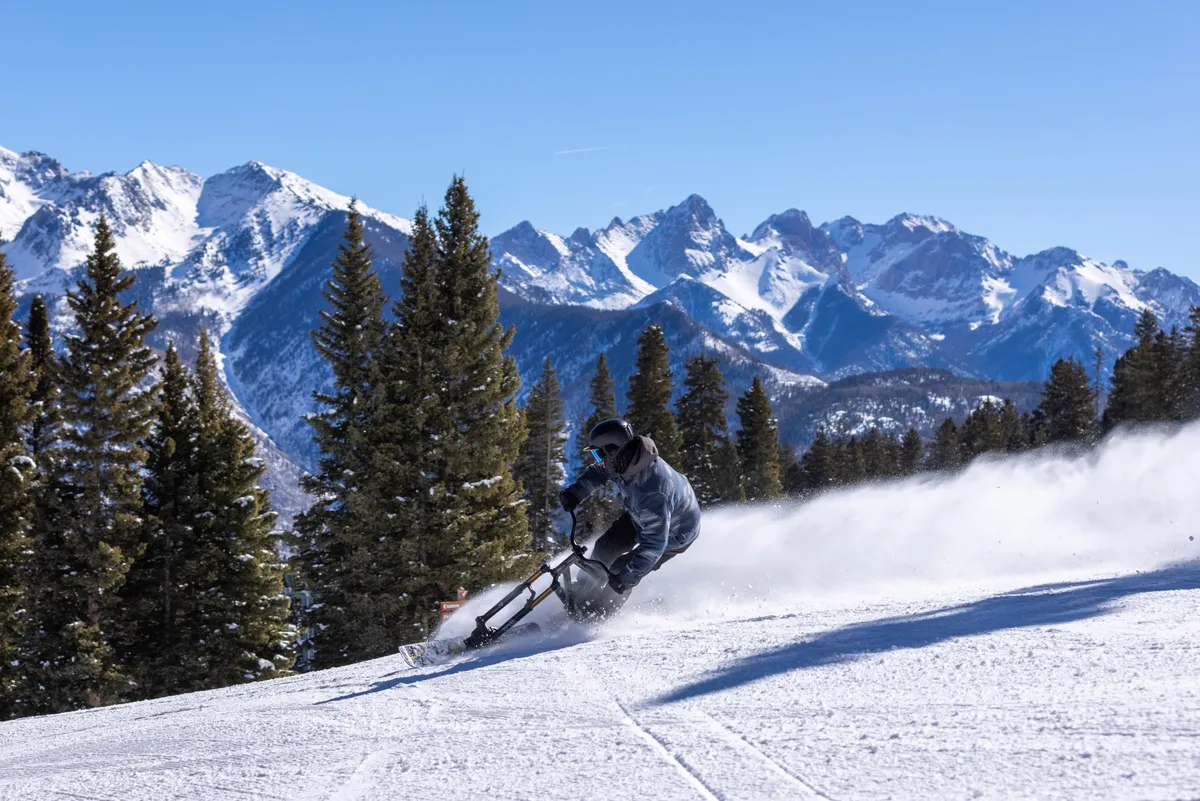 A dynamic exterior shot featuring a skier speeding down a snowy mountain, surrounded by pine trees. The scene captures the thrill of winter sports in Durango and hints at the après-ski social experiences available nearby.