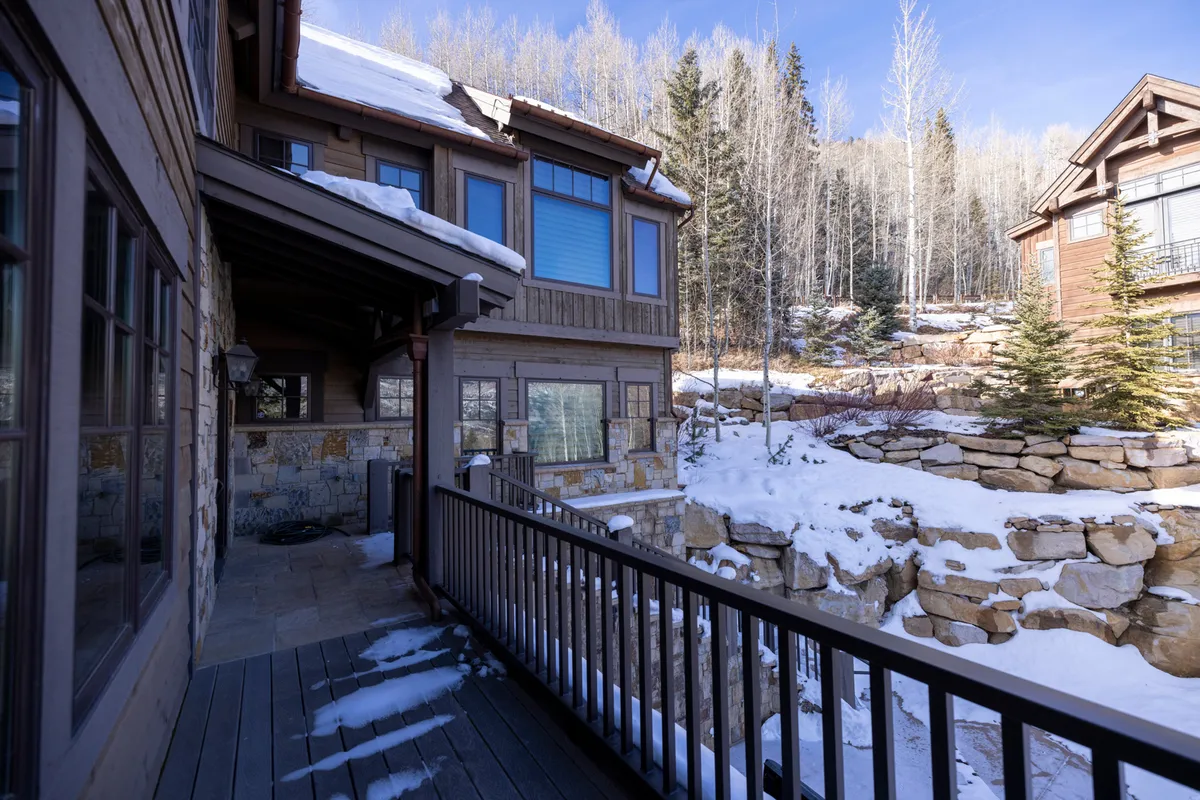 An inviting wooden deck outside a luxury mountain home, bordered by stone walls and snowy terrain, with trees in the background. The tranquil setting is perfect for relaxing after a day’s adventure—whether watching snowfall, stargazing, or gathering with friends.
