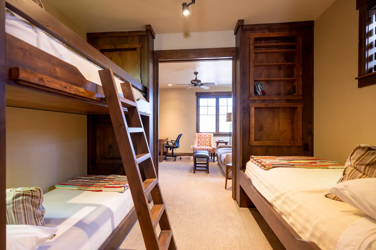 A cheerful bunk room featuring twin-over-twin bunk beds, a ladder, and an armchair, complemented by a small desk area. The layout is playful yet practical, ideal for younger guests or group stays.